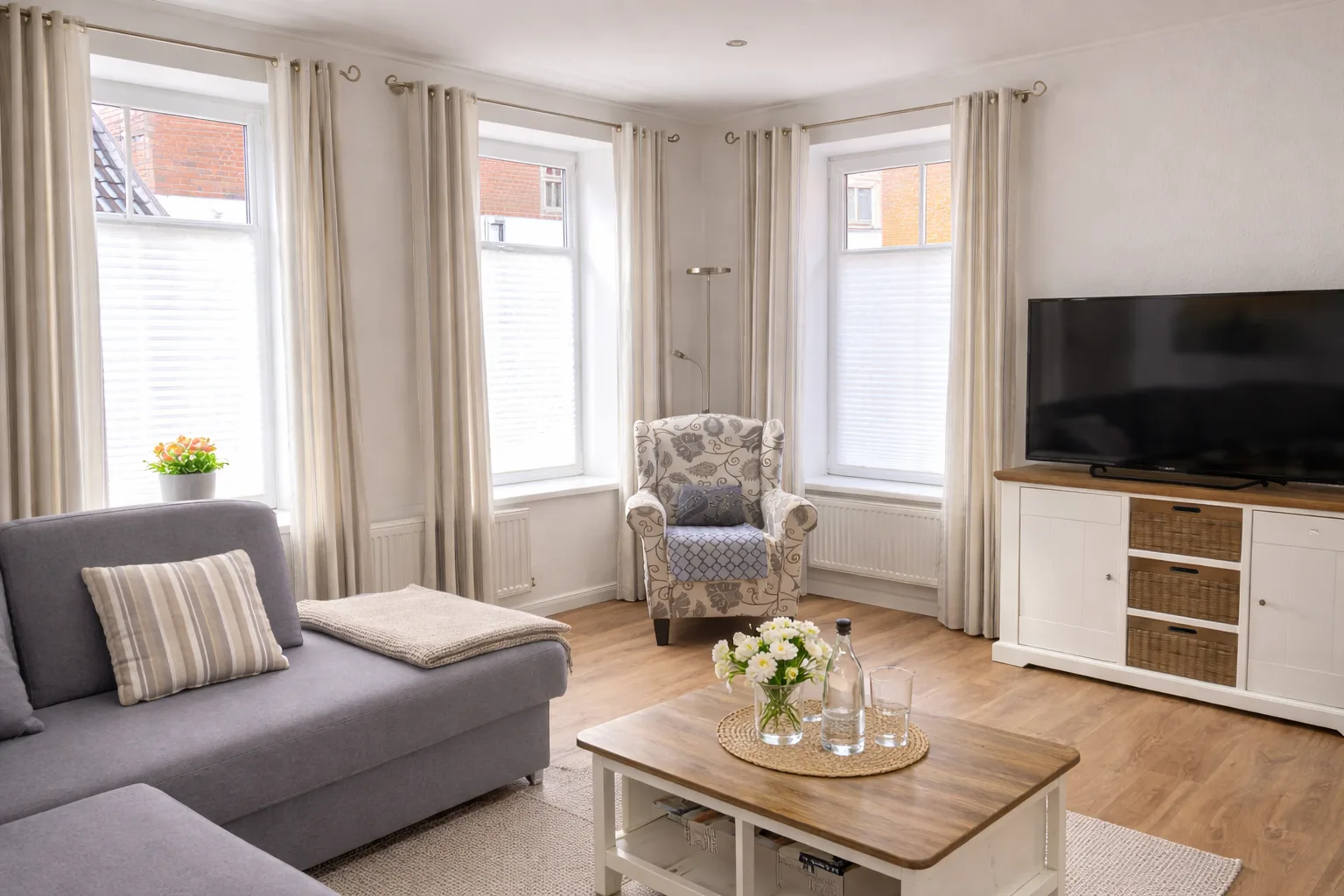 Wohnzimmer mit Smart-TV, Ohrensessel und großen Fenstern